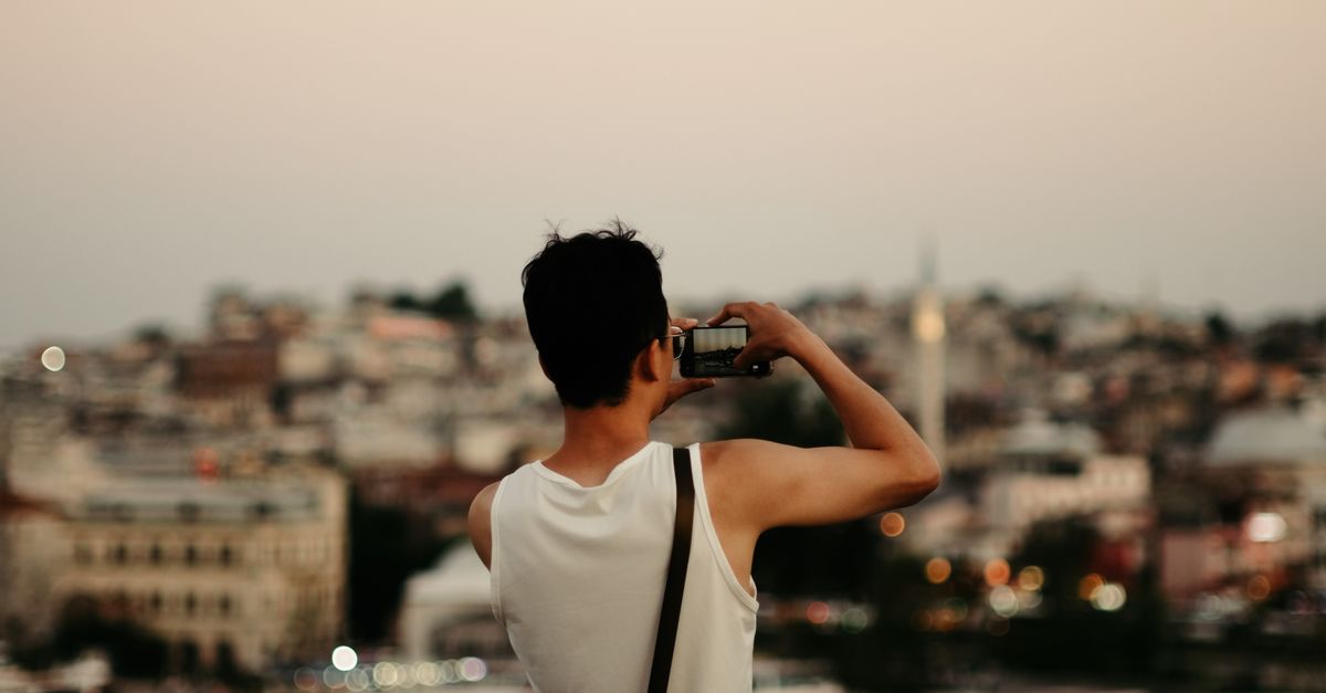 A man photographs the Istanbul skyline from a balcony at twilight, with city lights twinkling.