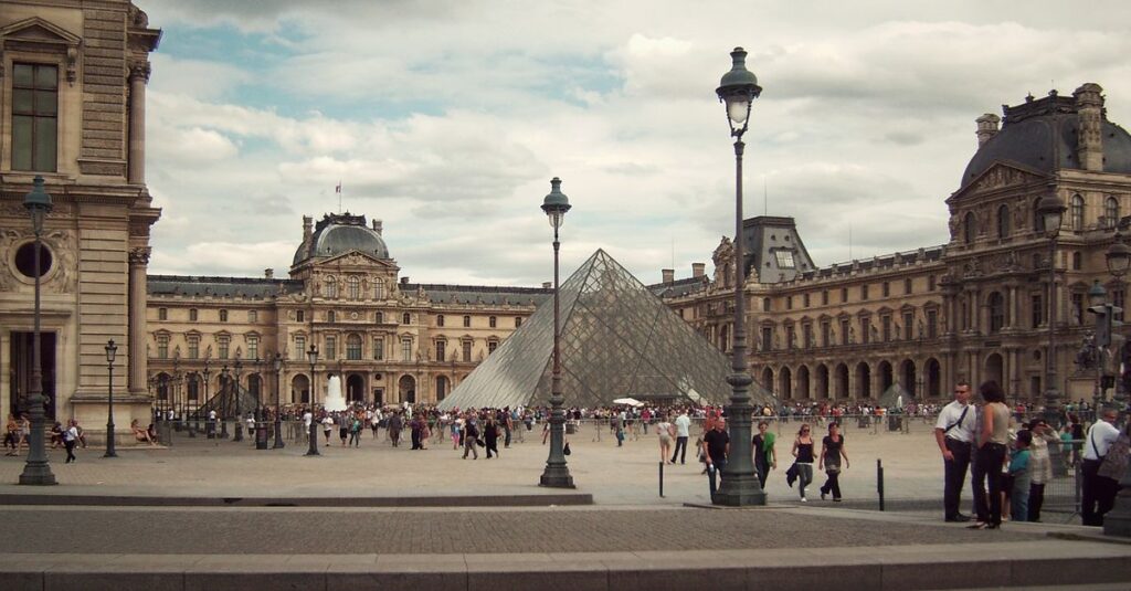 Crowds at the iconic Louvre Museum and its modern glass pyramid in Paris, France.