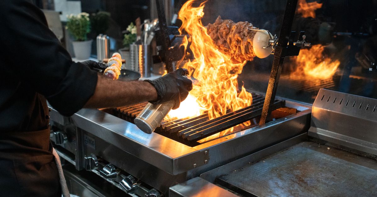 Chef grilling meat with spectacular flames in a modern kitchen setup.